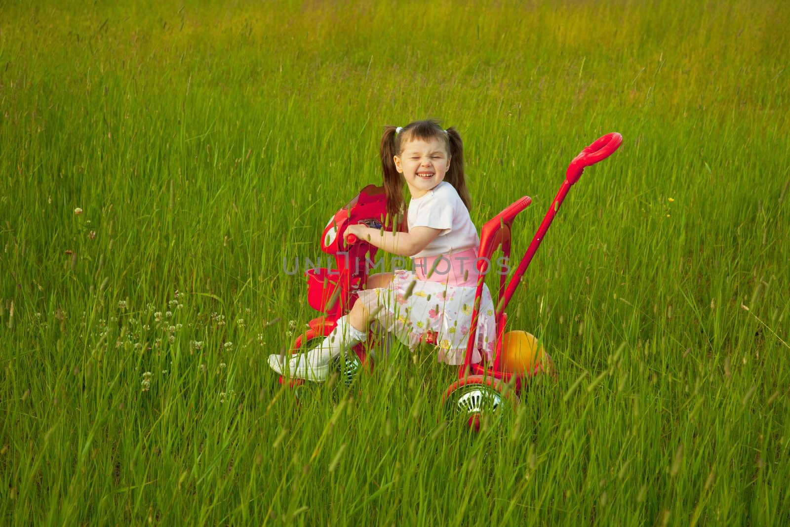 The comical child goes across the field on a bicycle and grimace