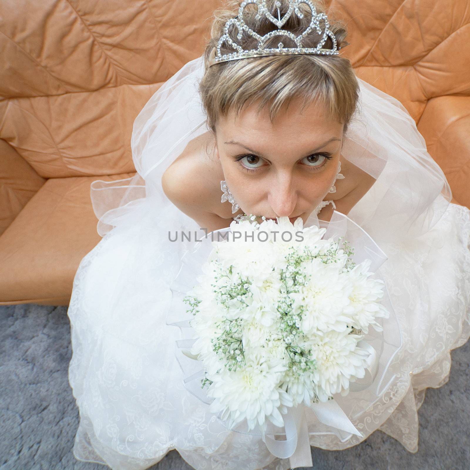 The amusing bride sits on a sofa with a bouquet - the top view