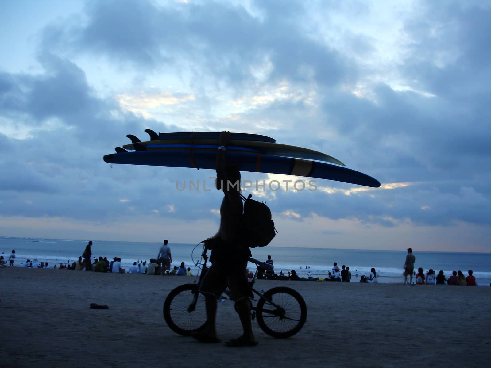 A man carrying surfboards on the beach at dusk, Kuta, Bali, Indonesia.