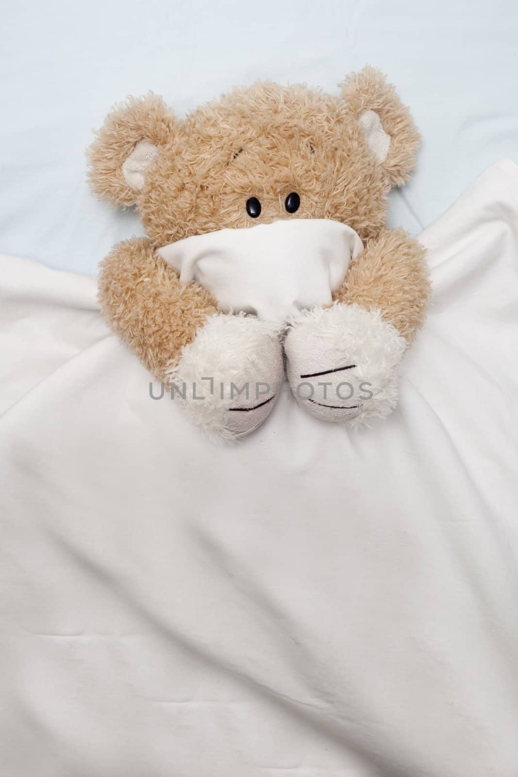 An adorable teddy bear laying in bed, scared, under the sheets.