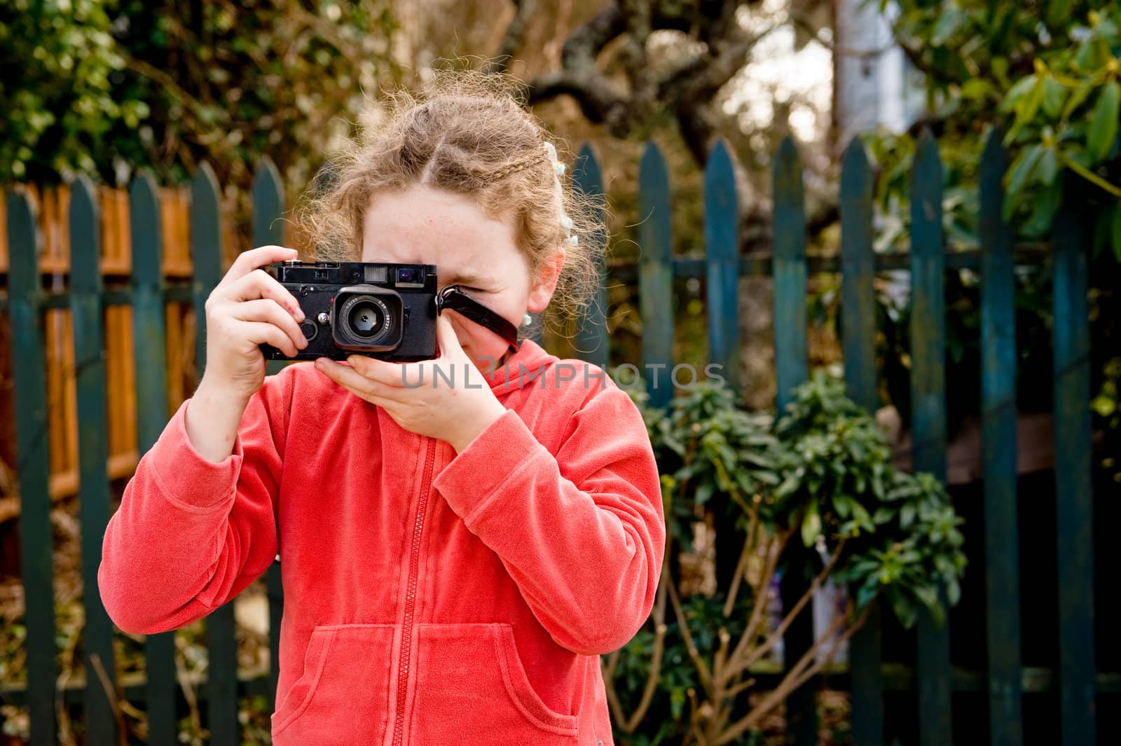 young girl taking photo towards camera, fence behind