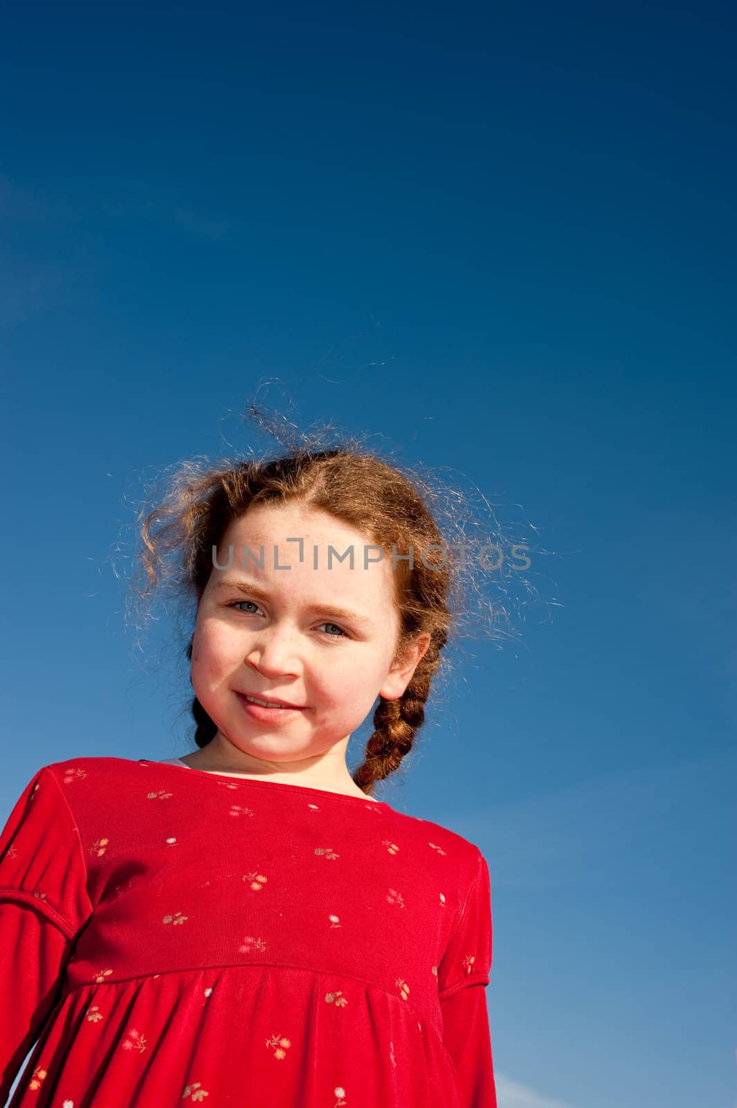young girl looking down into camera, blue sky behind