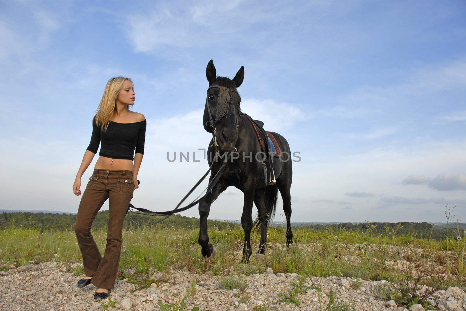 blond teenager and her black horsewalkin  in the nature