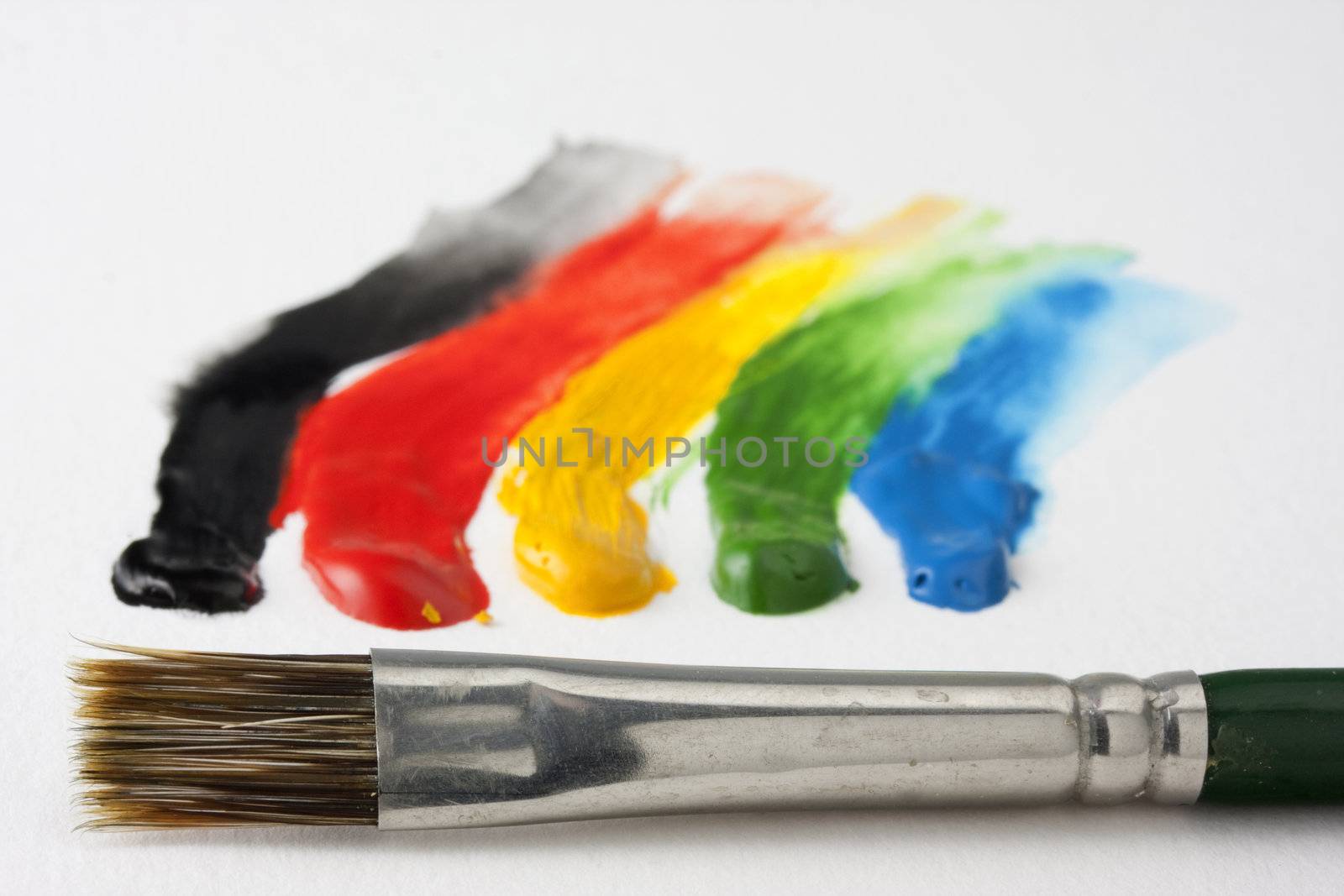 small paintbrush and 5 dabs (black, red, yellow, green, blue) of watercolor paint with smudges going out of focus on white textured paper