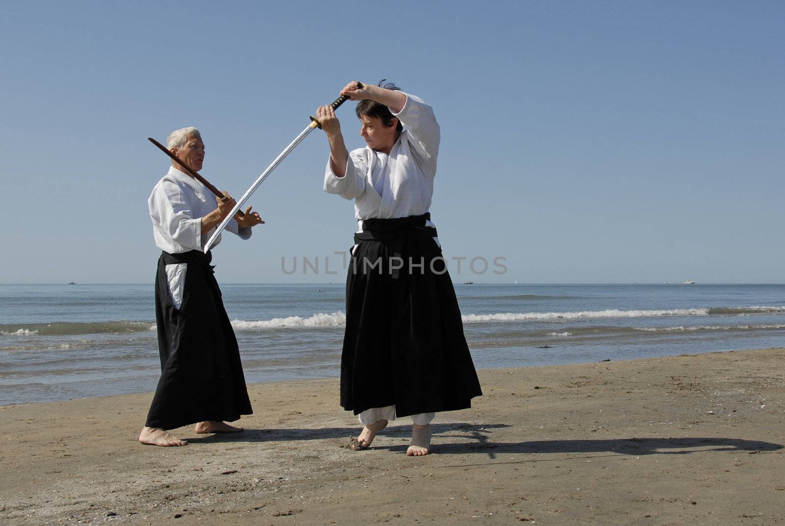 Two adults are training in Aikido on the beach