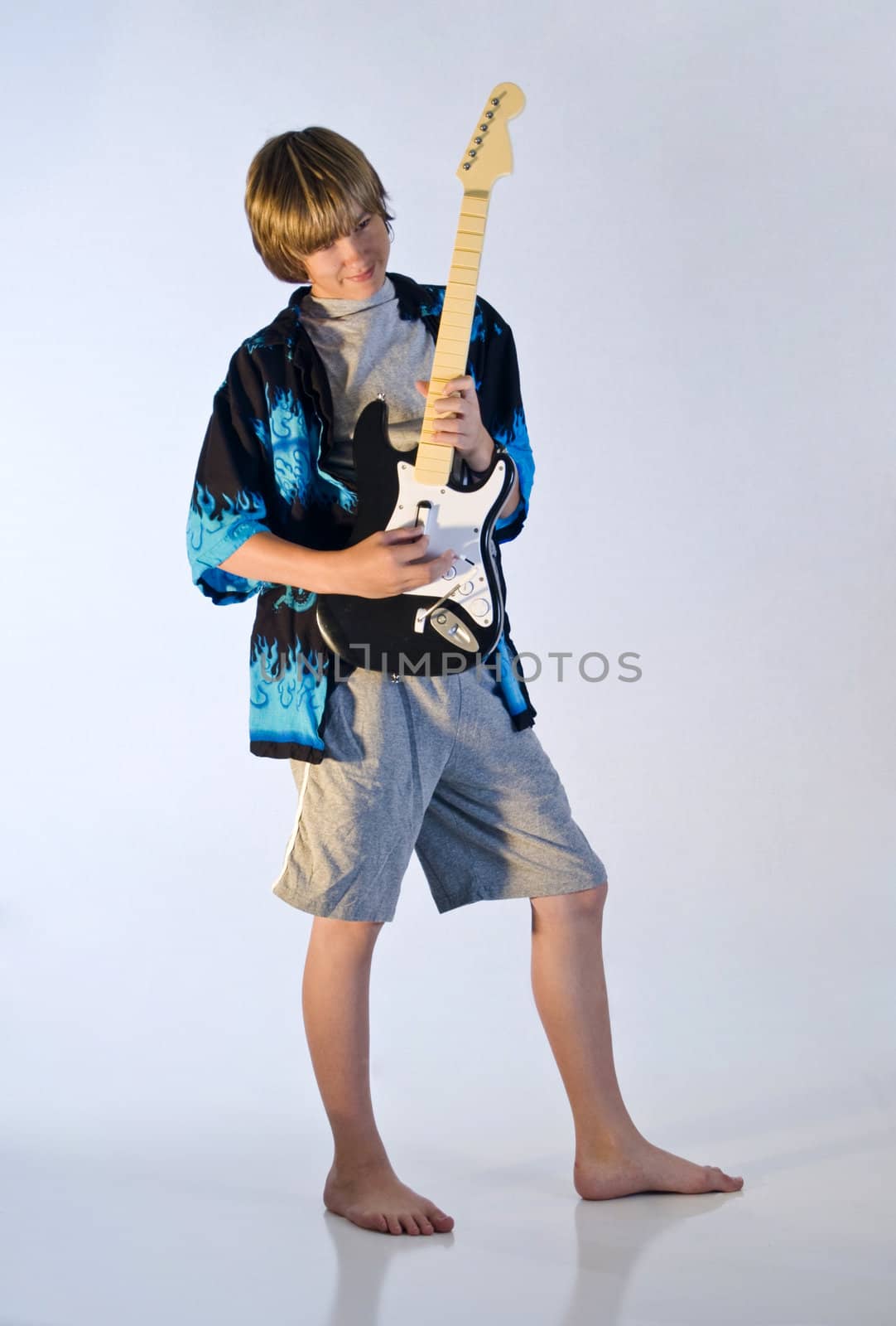 Teenager playing a video game guitar while standing on a reflective surface.