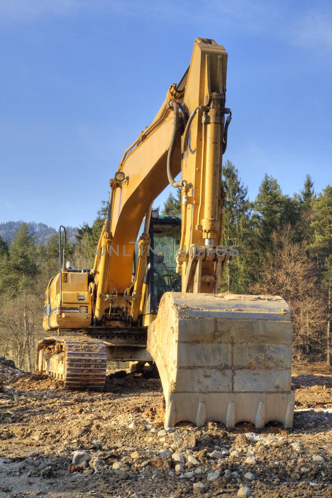 Yellow dredger on construction ground against forest and sky.