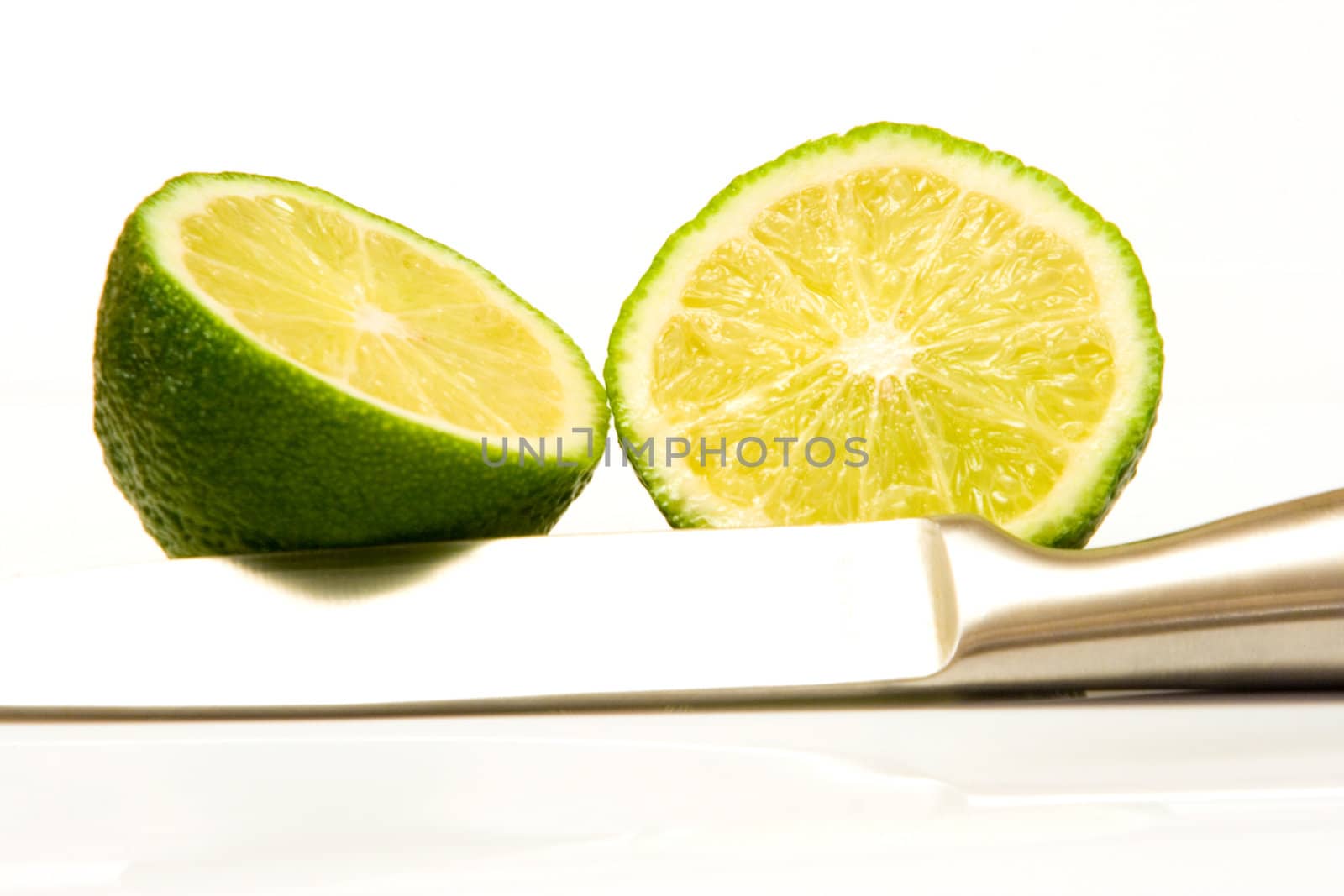 high key image of a sliced lime and a stainless steel knife on a white background