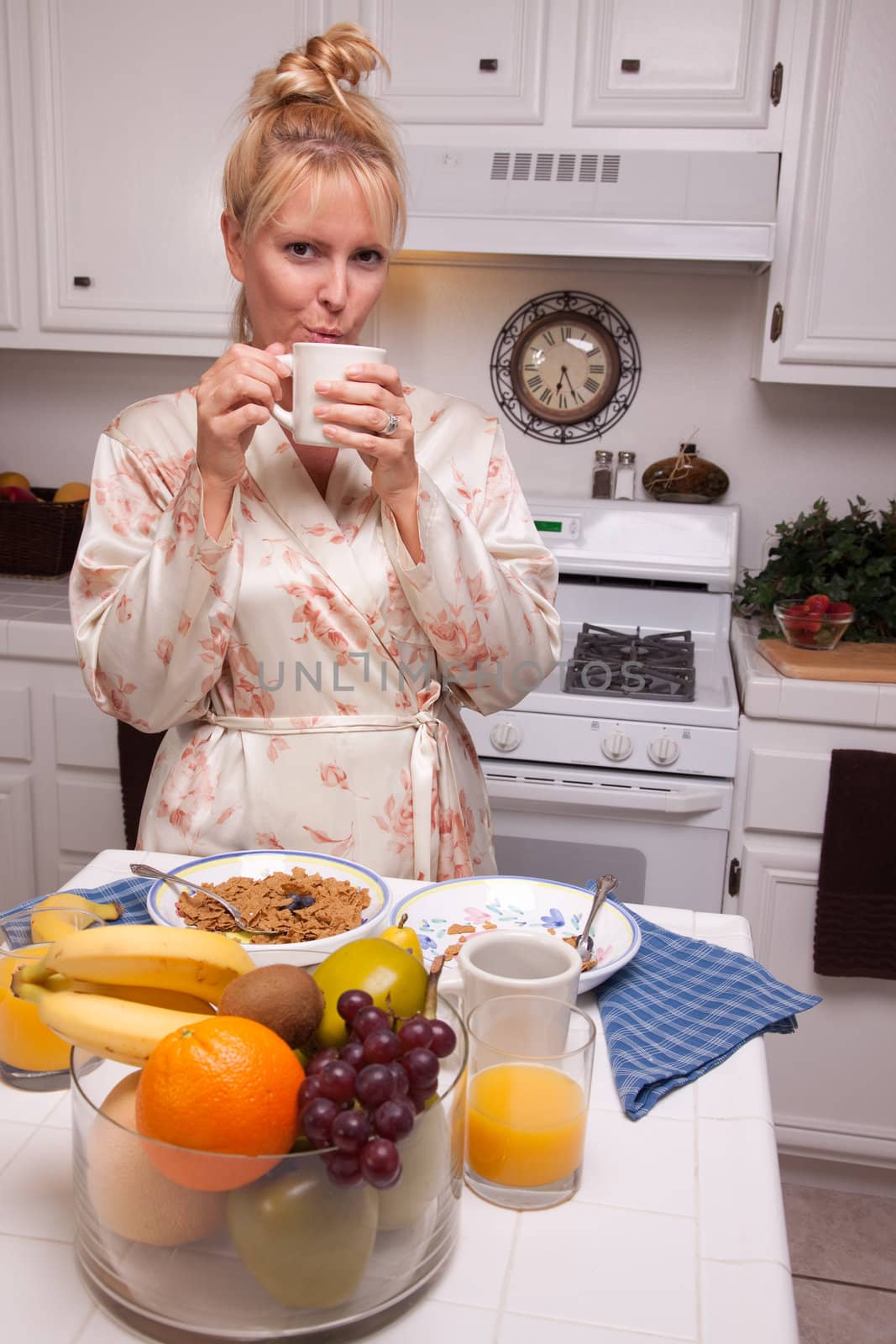 Attractive Woman In Kitchen with Fruit, Coffee, Orange Juice and Breakfast Bowls.
