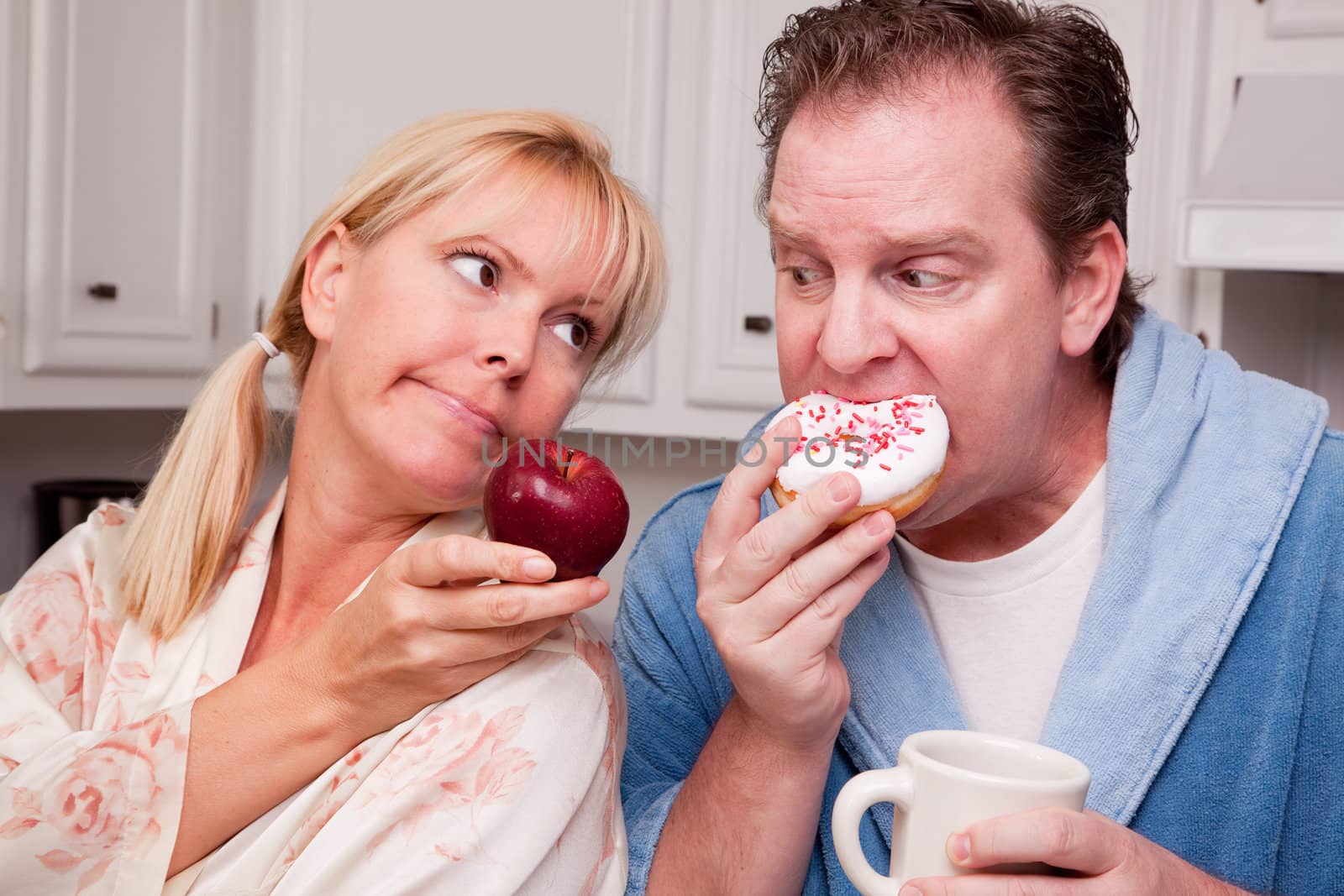 Couple in Kitchen Eating Donut and Coffee or Healthy Fruit.