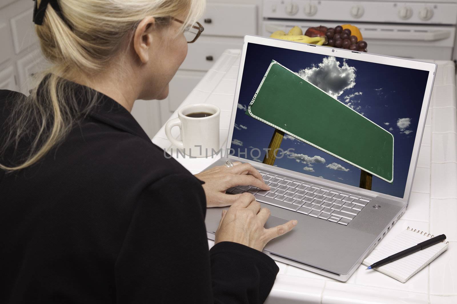 Woman In Kitchen Using Laptop with Blank Road Sign Ready for Your Own Message. Screen can be easily used for your own message or picture. Picture on screen is my copyright as well.