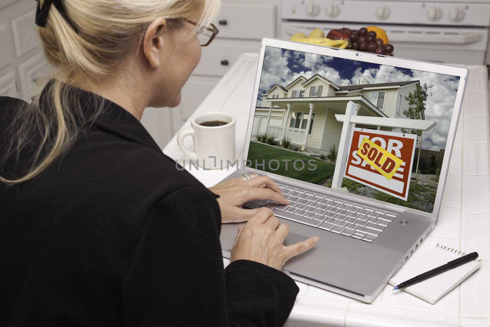 Woman In Kitchen Using Laptop to Research Real Estate. Screen can be easily used for your own message or picture. Picture on screen is my copyright as well.