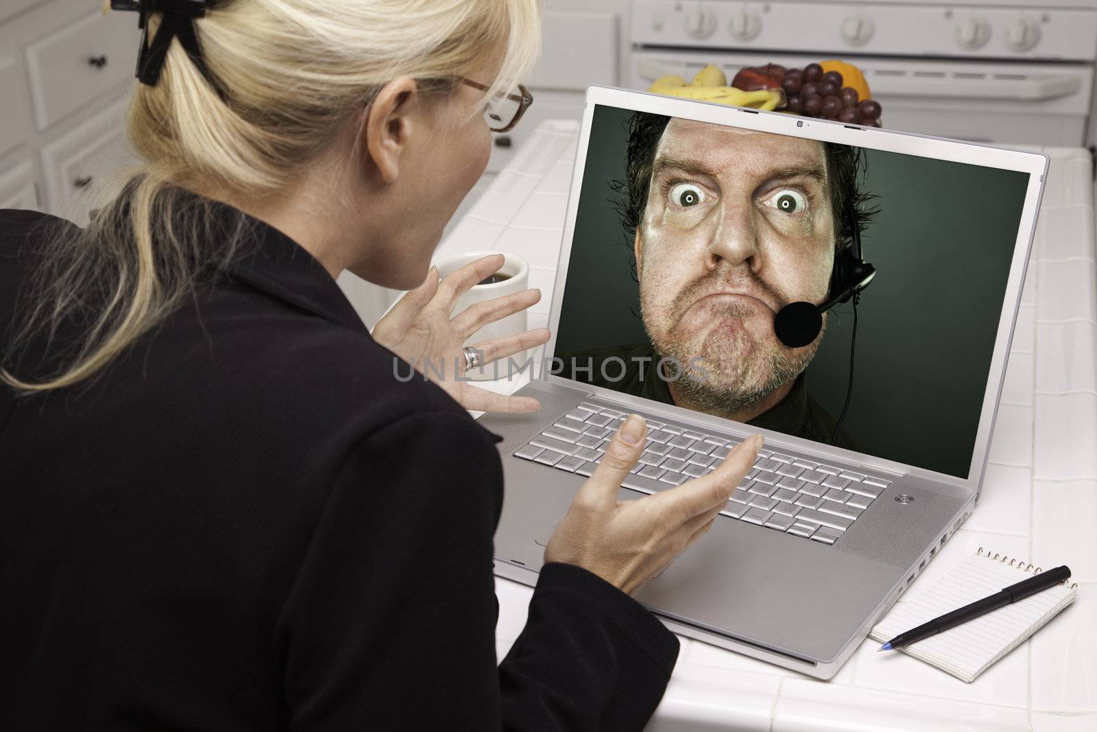 Shocked Woman In Kitchen Using Laptop with Grumpy Customer Support Man On Screen. Screen can be easily used for your own message or picture. Picture on screen is my copyright as well.