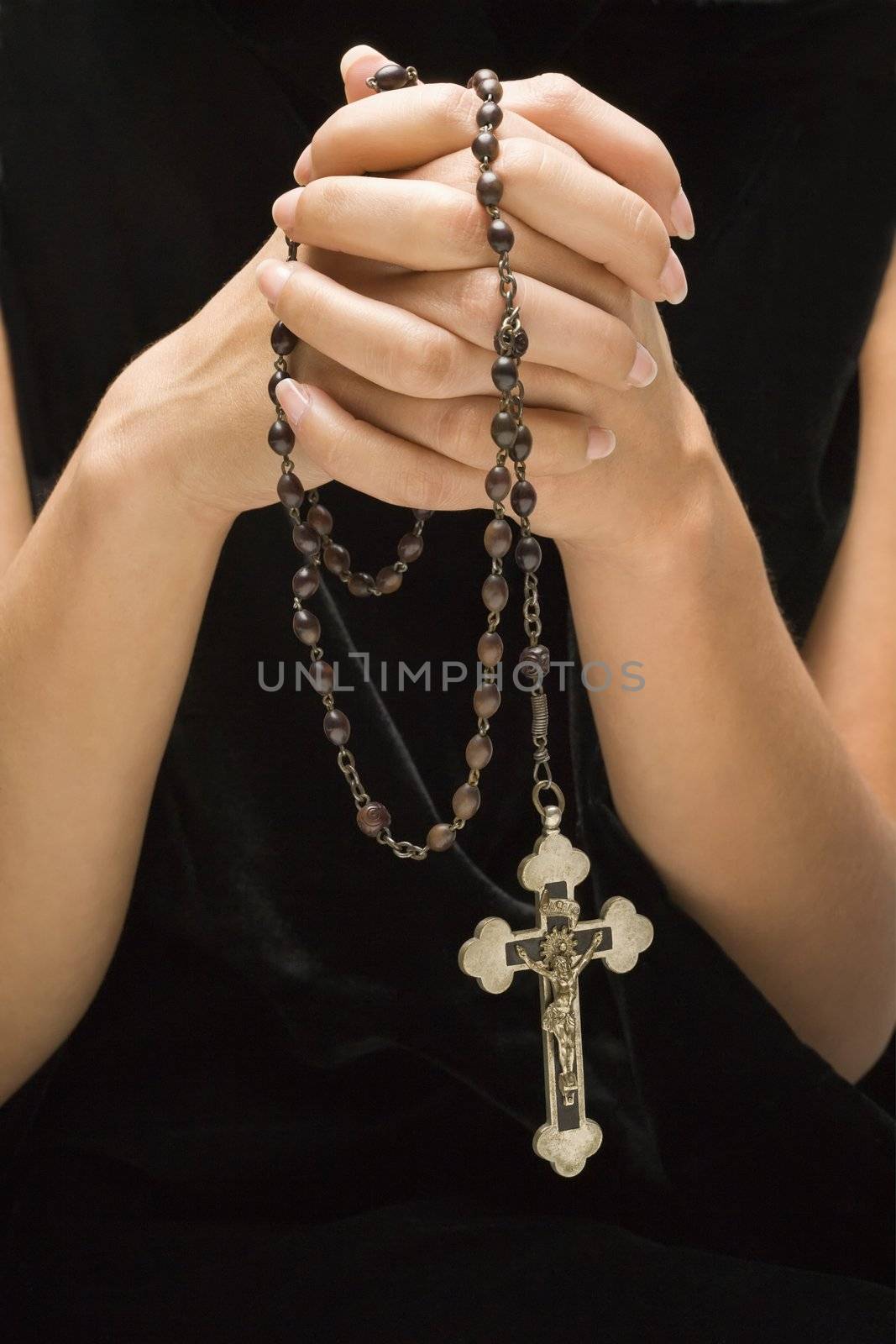 Woman holding rosary with hands clasped together.