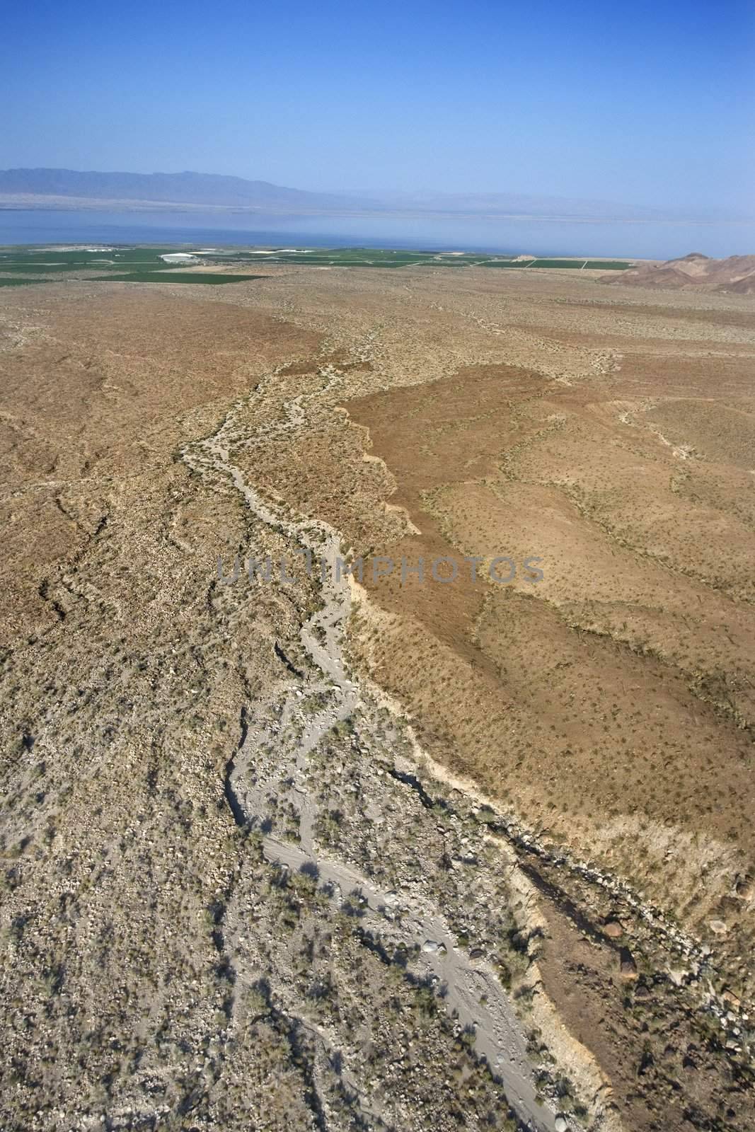 Aerial view of desert with lake and mountains in background.