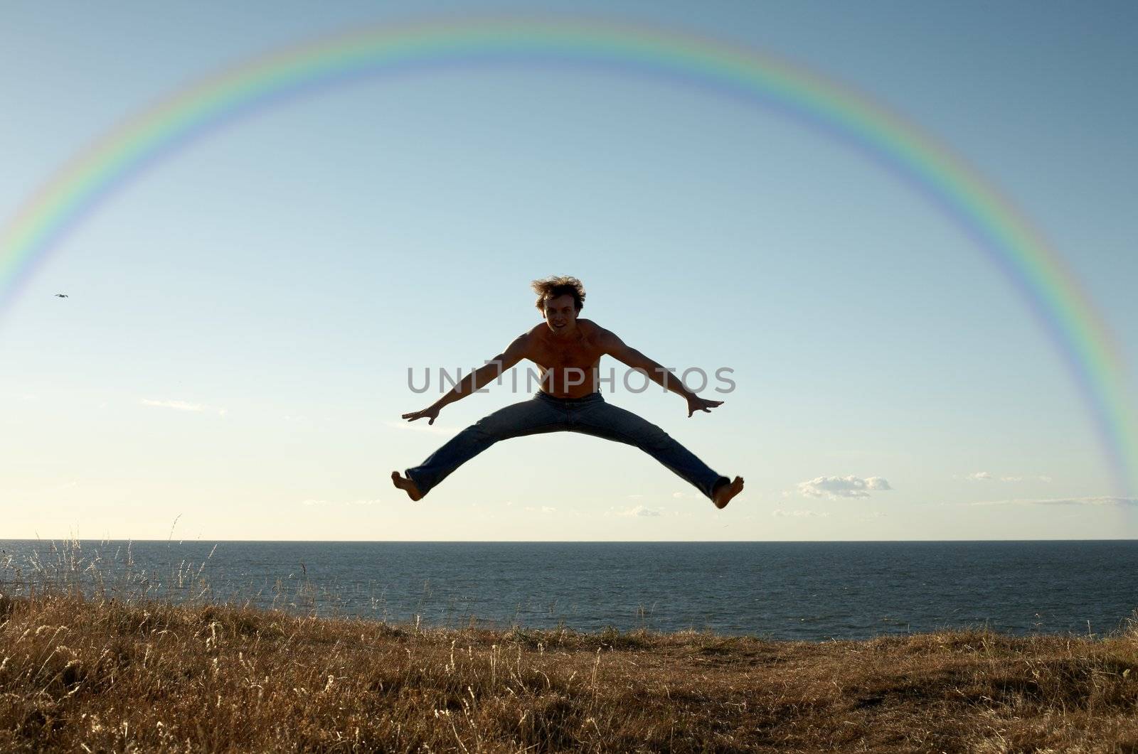 sporty man jumping under big colorful rainbow