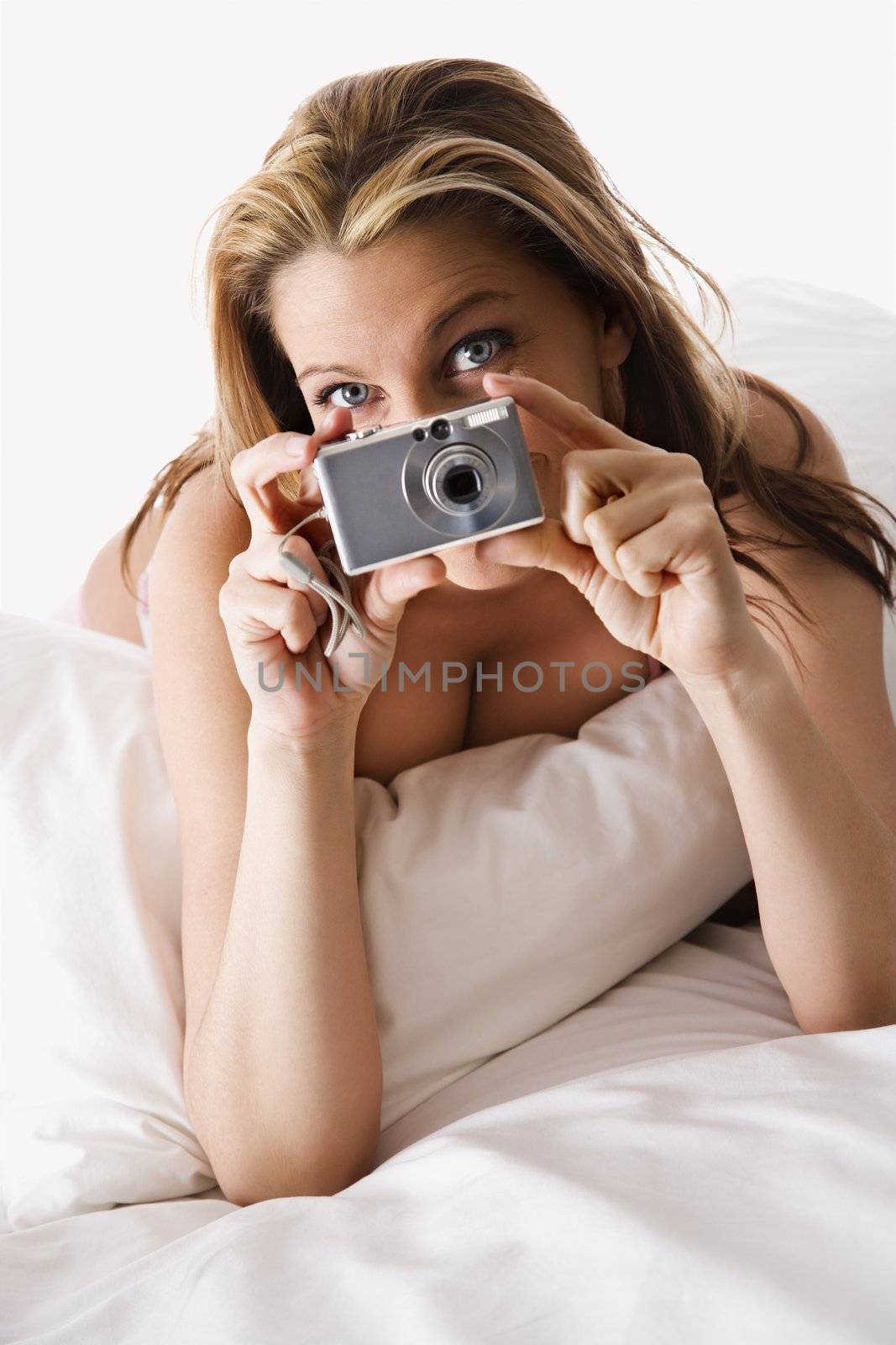 Sexy Caucasian woman lying on bed pointing camera at viewer.