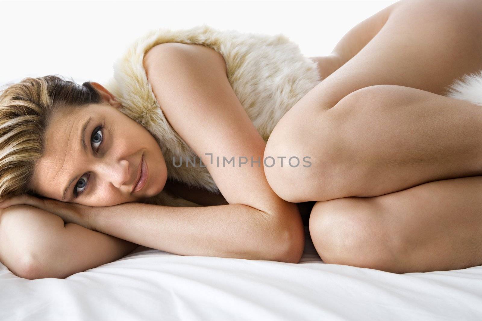 Caucasian woman lying curled up on bed looking at viewer.