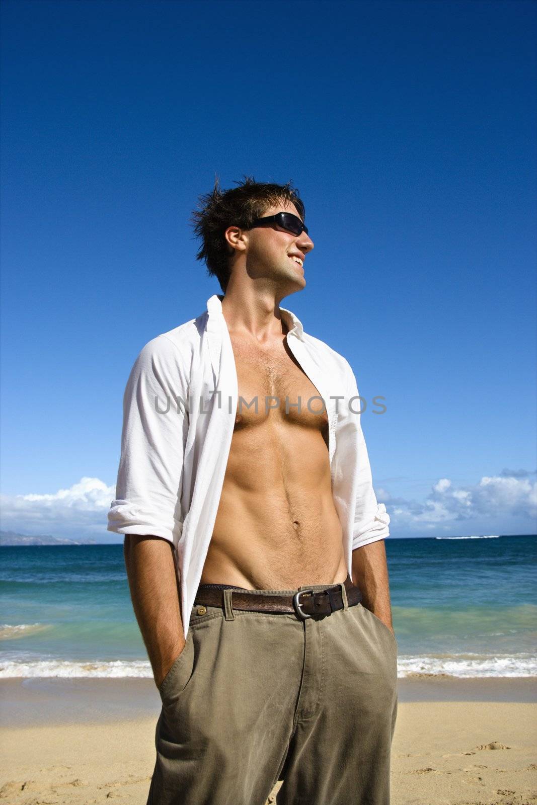 Portrait of attractive man standing with shirt unbuttoned wearing sunglasses on Maui, Hawaii beach.