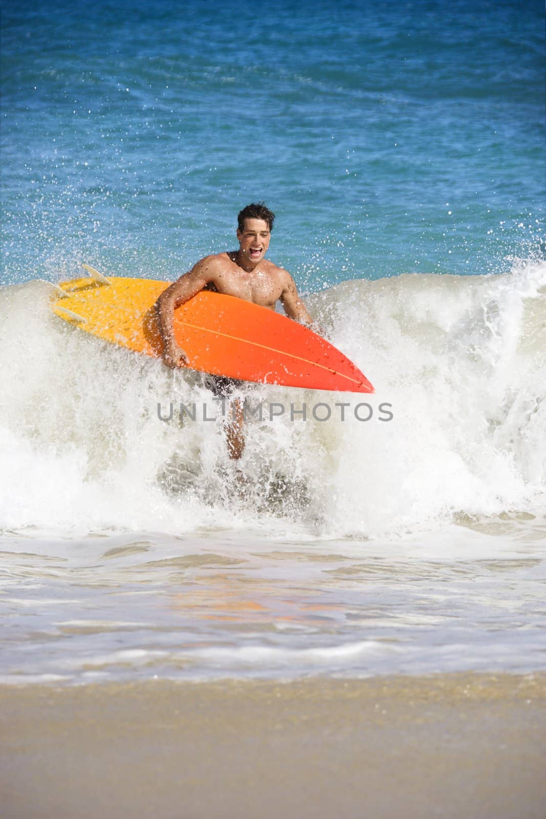 Attractive young man running out of water carrying surfboard in Maui, Hawaii.