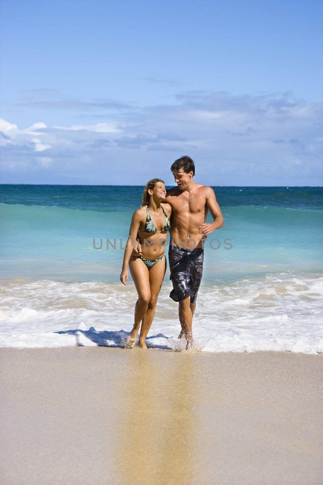 Attractive couple embracing and smiling as they walk out of water in Maui, Hawaii.