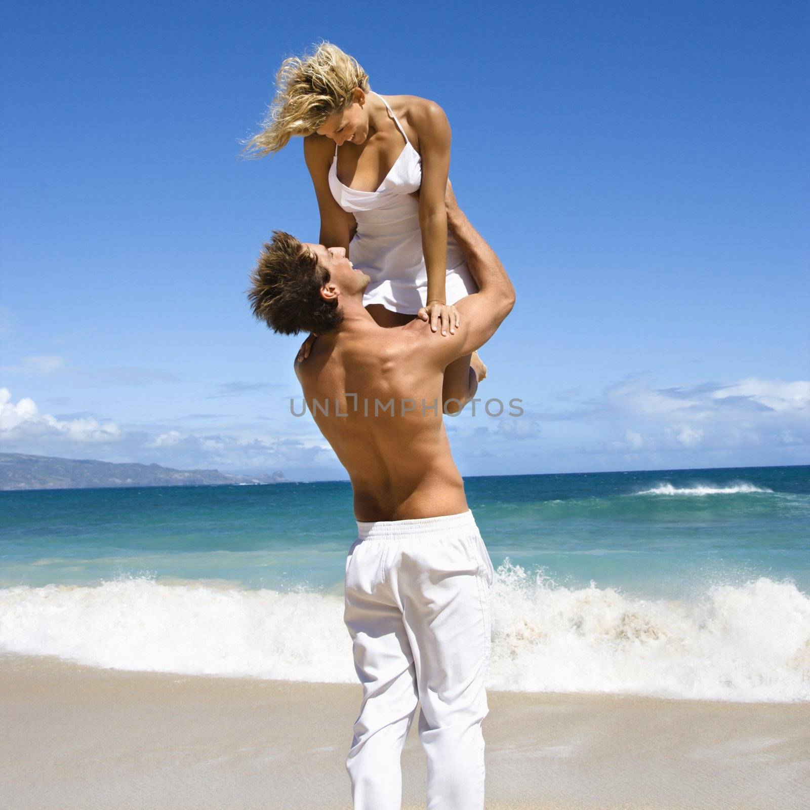 Man holding woman up in air as they look into eachother's eyes on Maui, Hawaii beach.