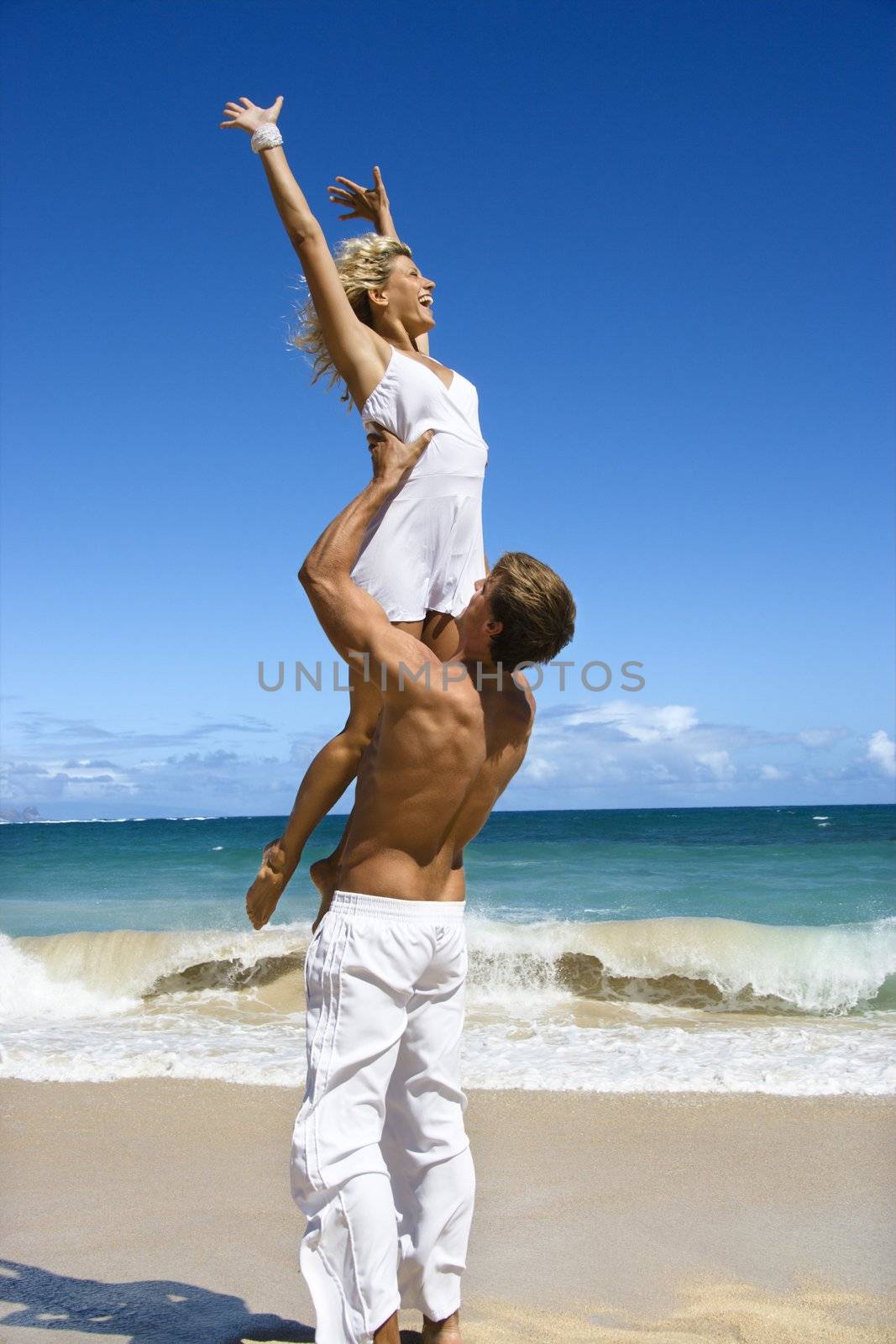 Man holding woman up in air on Maui, Hawaii beach.