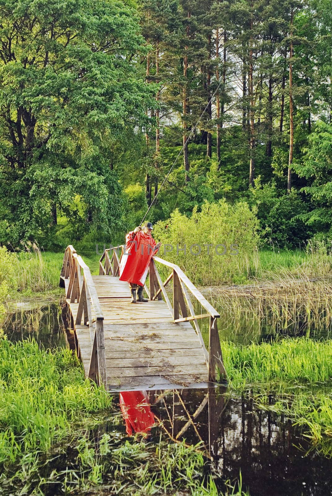 The fisher in a red raincoat on the wooden bridge leaving in water