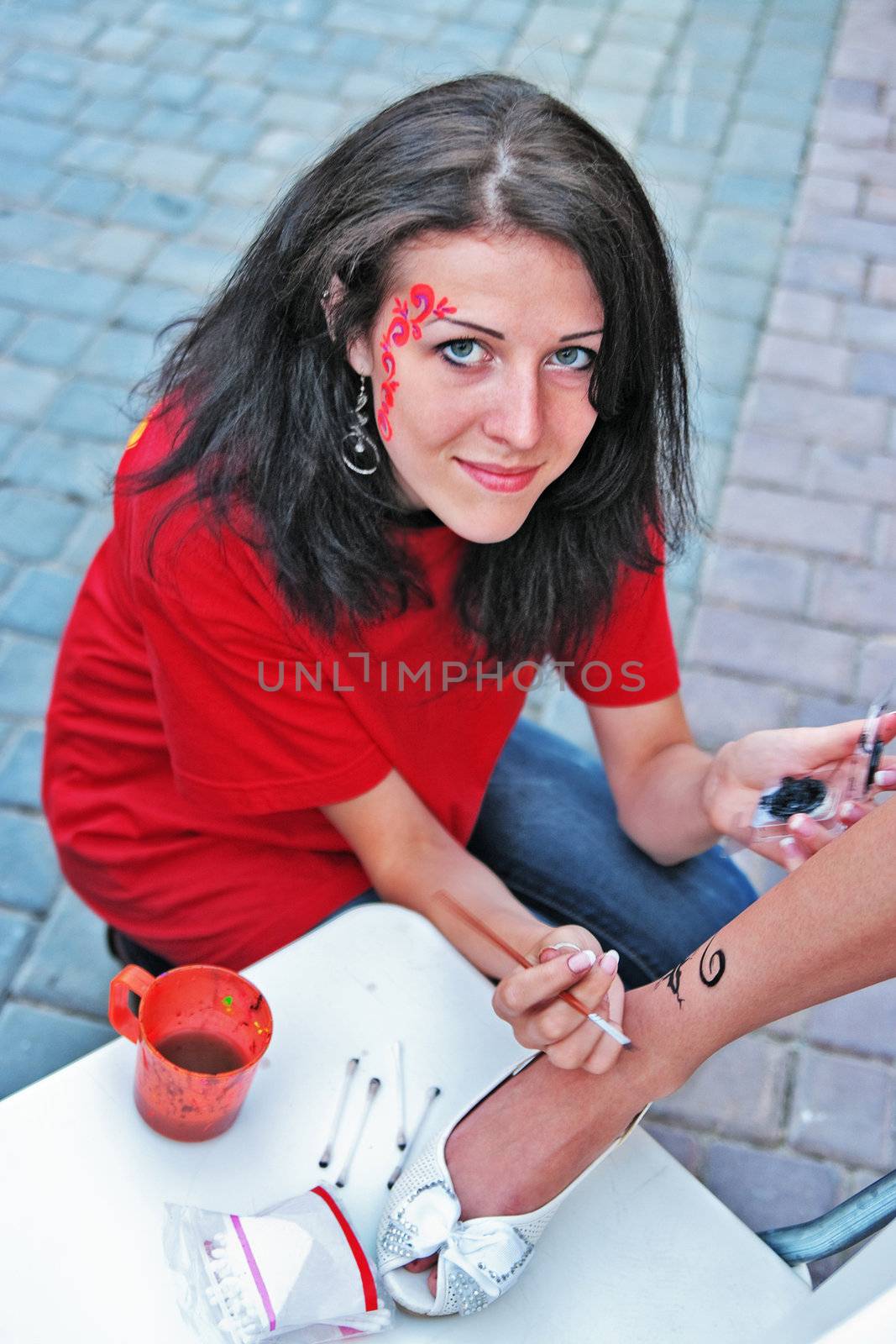 The young girl draws a tattoo  paint on a foot