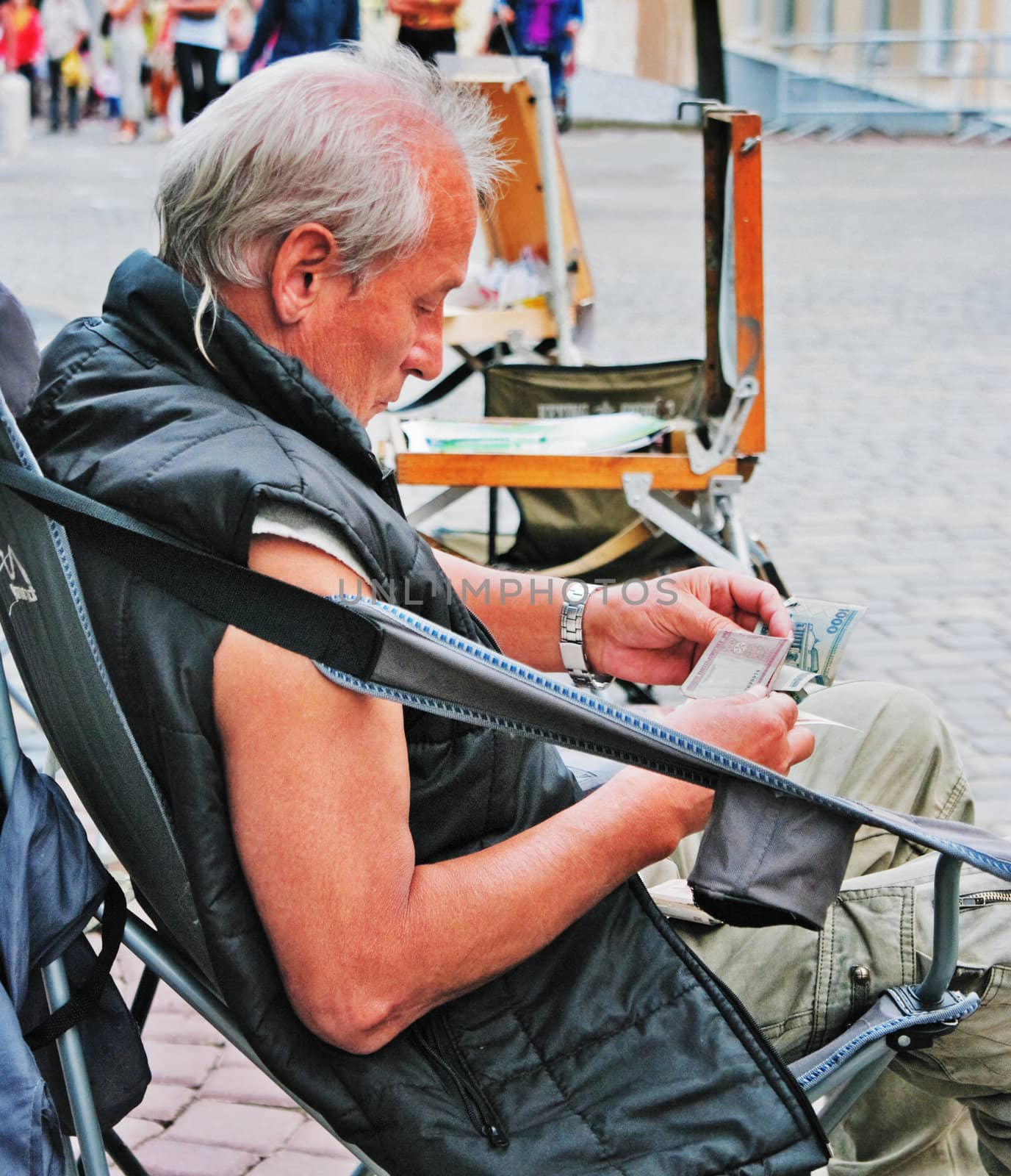 The street artist considers money sitting on an collapsible armchair