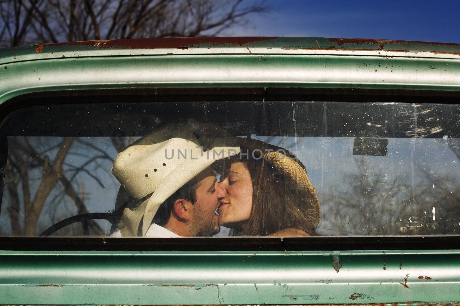 Cowboy and girlfriend kissing in through the back window of a pickup truck