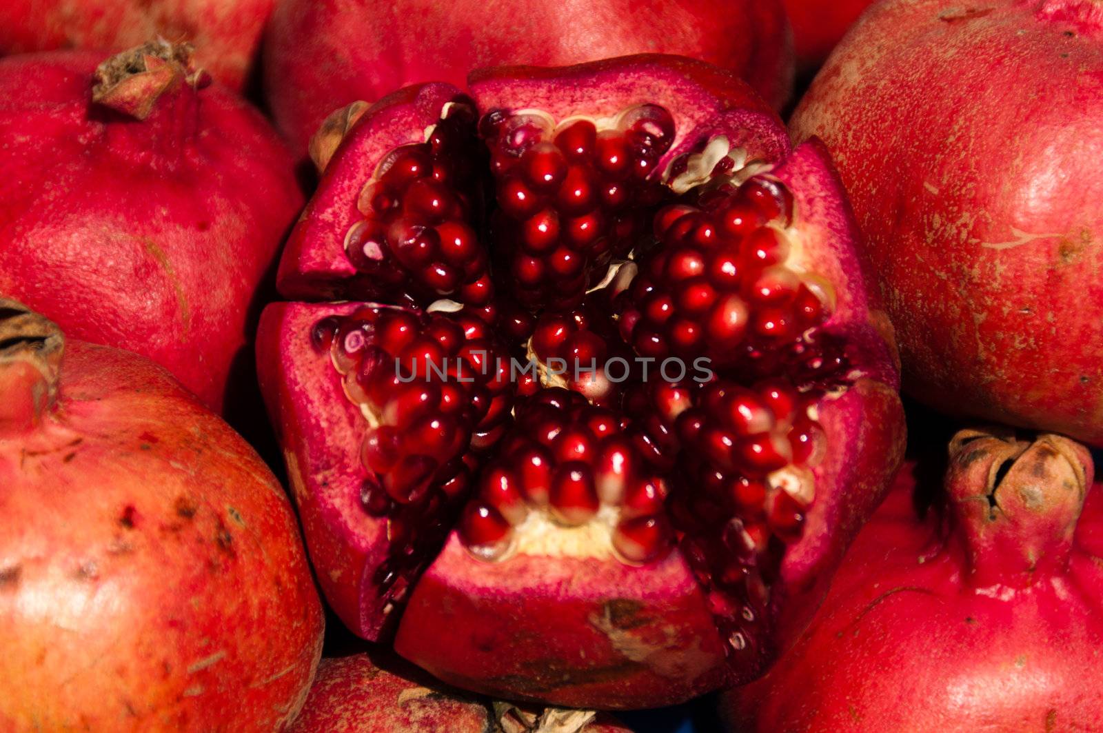 Closeup on several pomegranate fruits, the center one is cut in halves