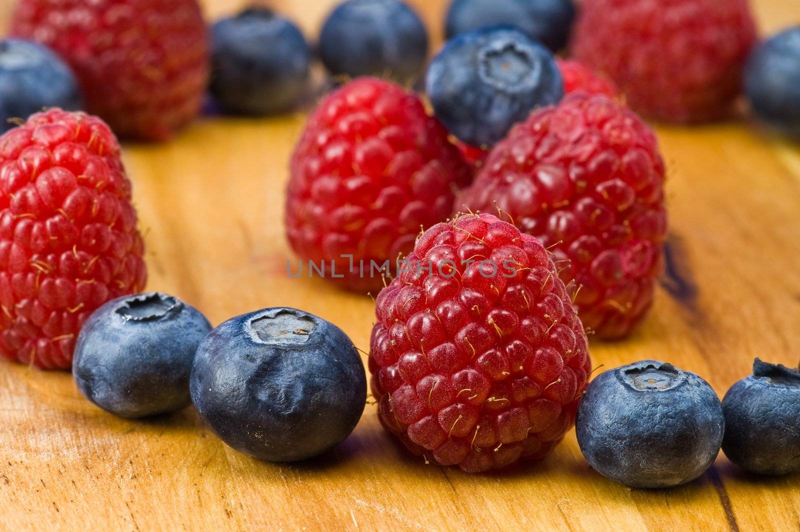 A couple of fresh ripe rasberry and blueberry on the wooden plate