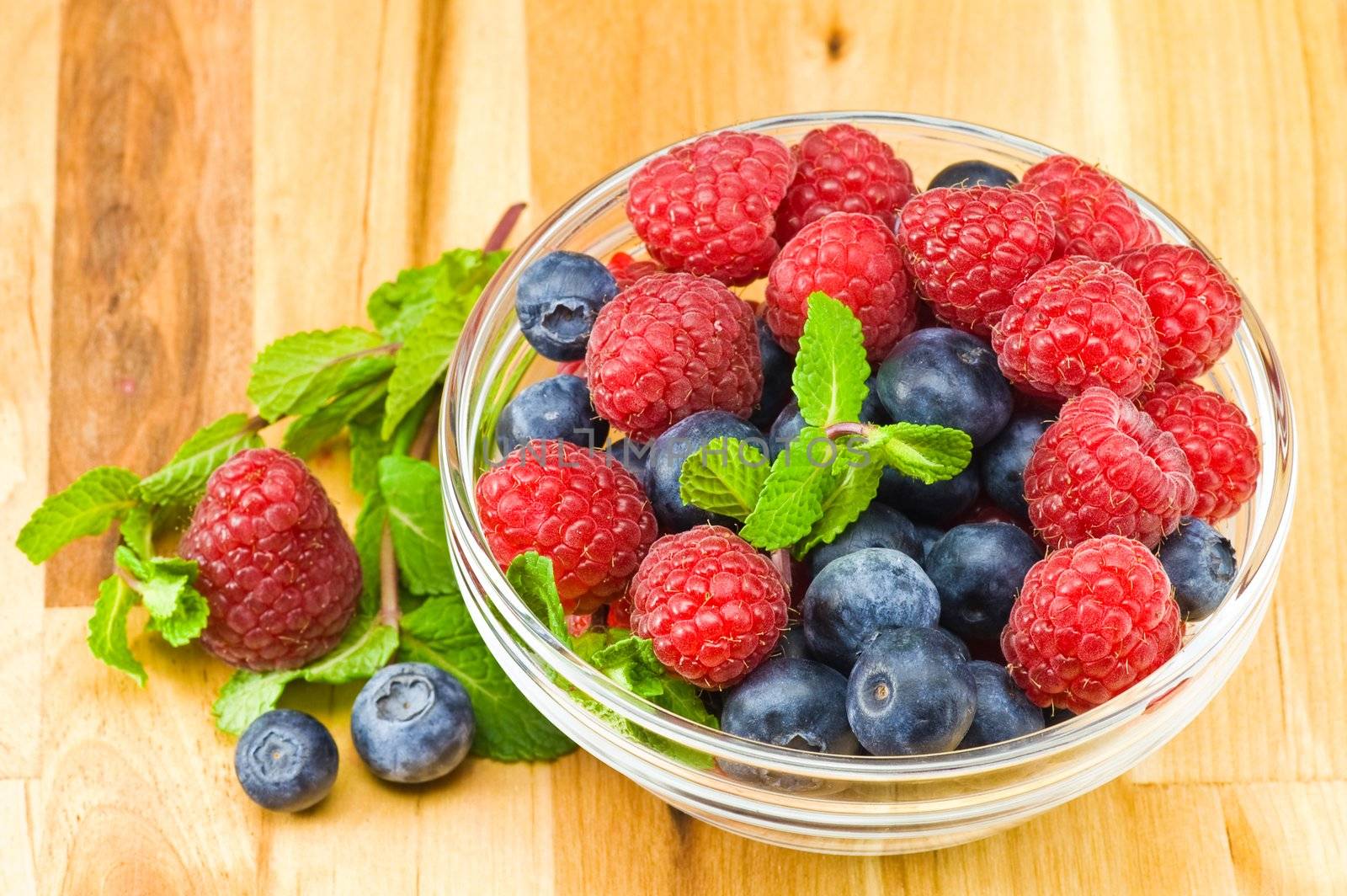 Fresh ripe raspberry and bluberry in glass jam-dish