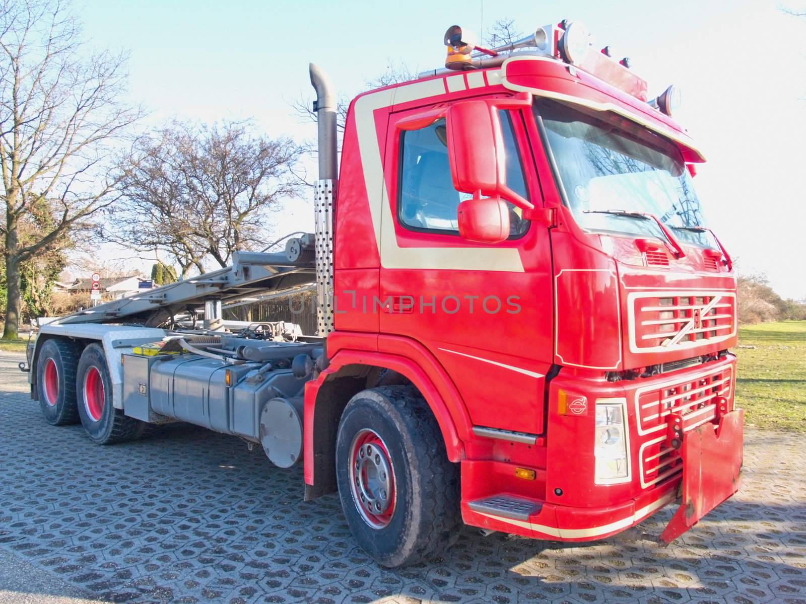 Front side view of red skip truck with hydraulic lifting  arm