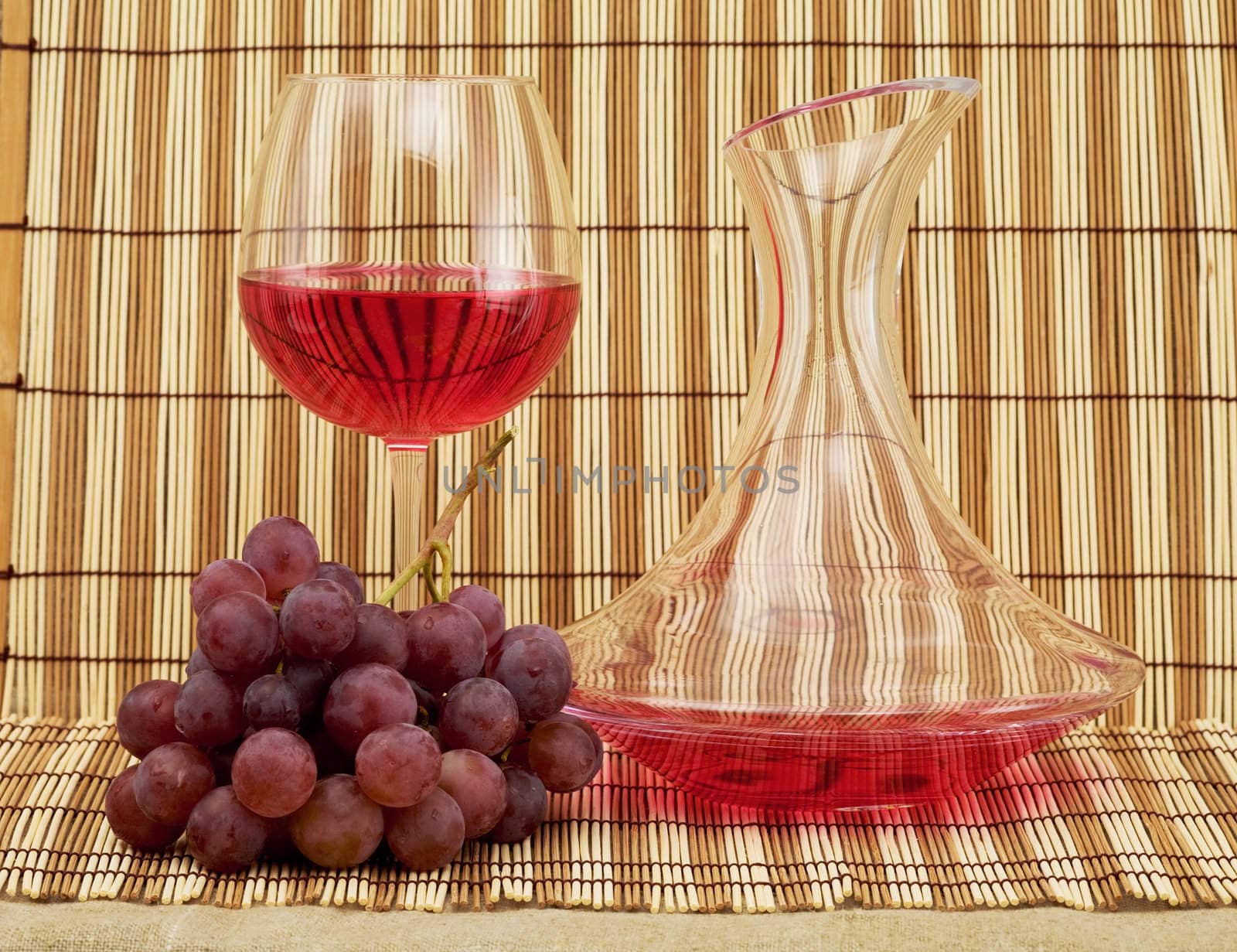 Still life with decanter, goblet and grapes on mat background