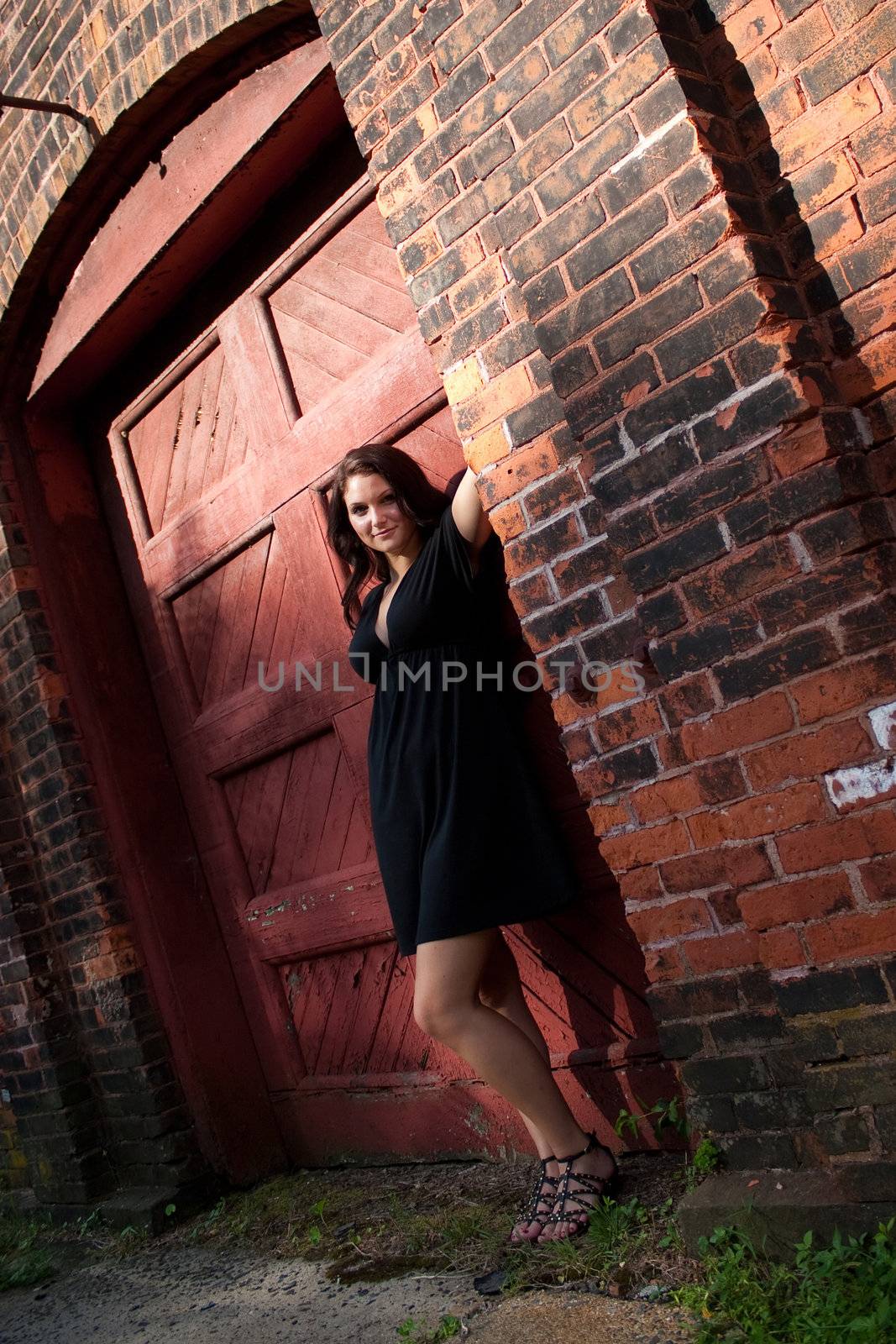A pretty young woman in a black dress posing in an old doorway.
