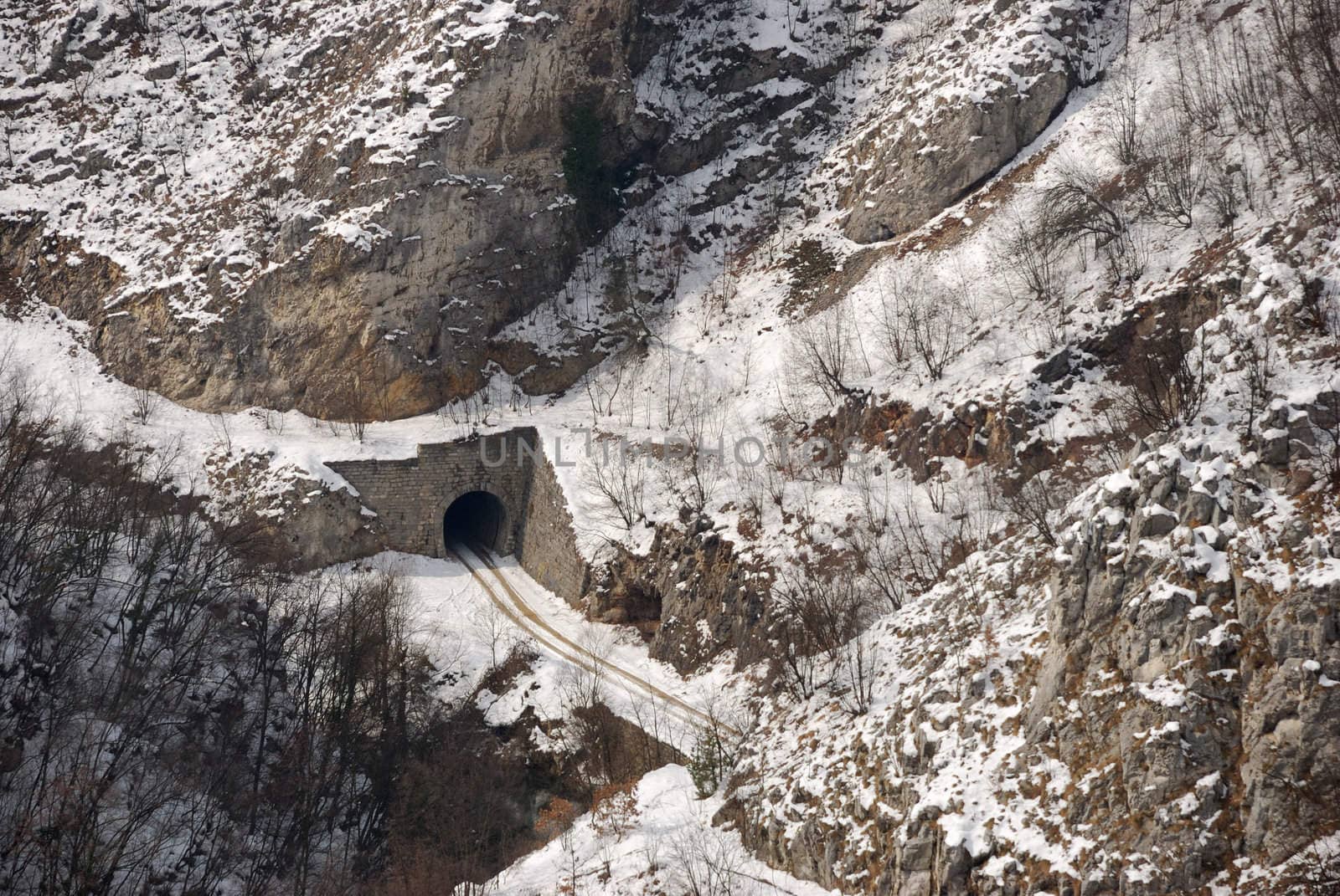 Tunnel in a hill and car trails in snow.