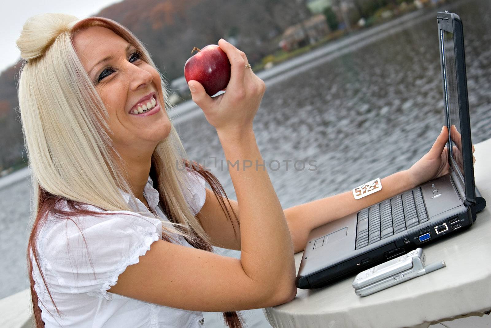 A beautiful young blonde woman in a mobile business setting eating a red apple.