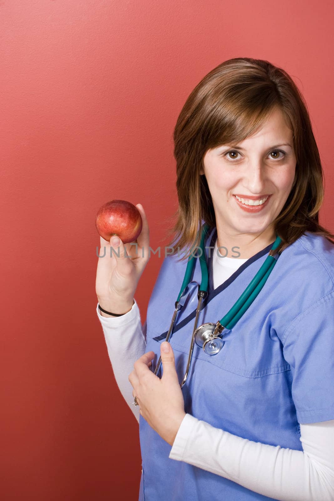 A young nurse is holding up an apple.  An apple a day keeps the doctor away.