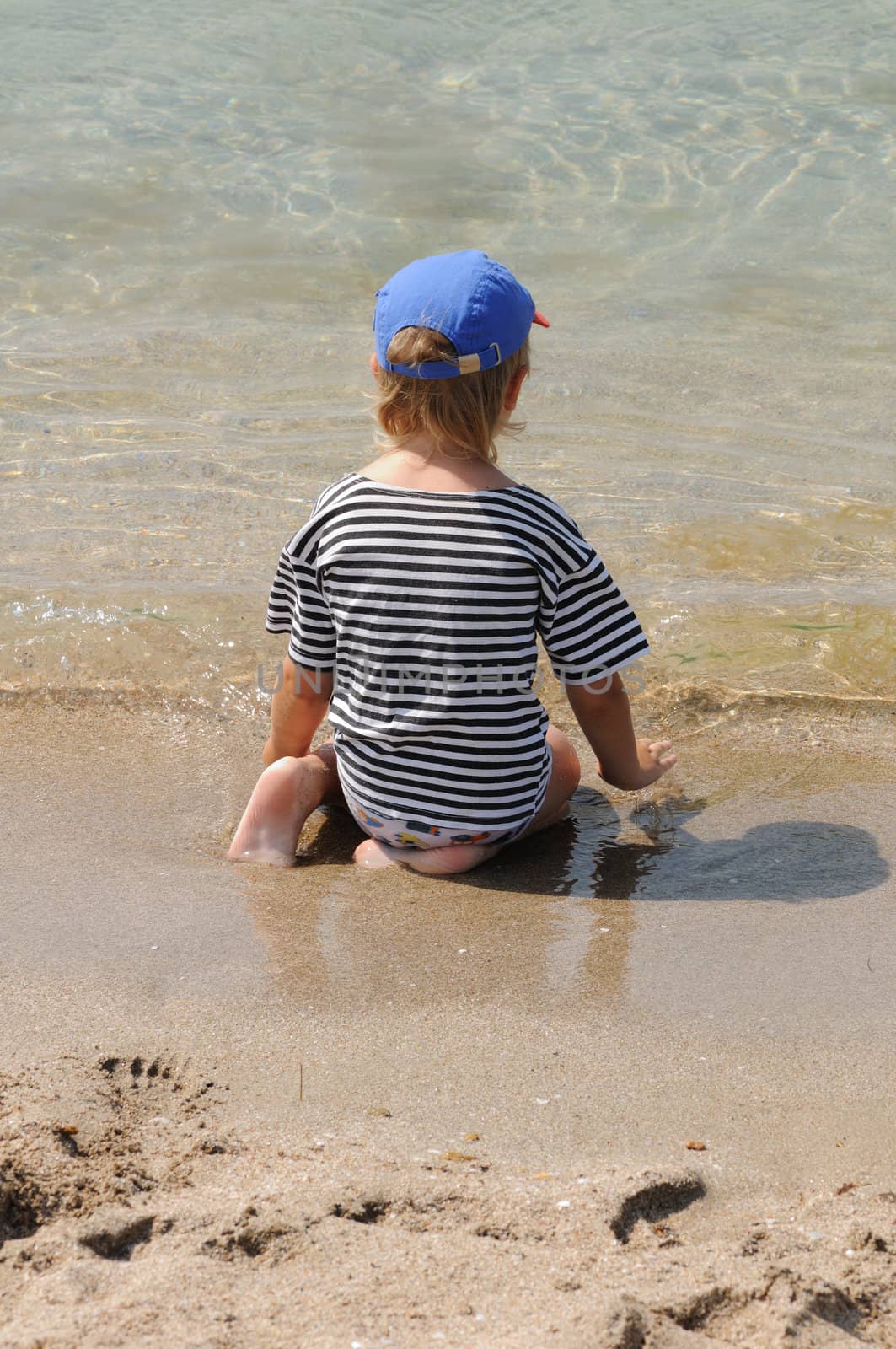 The child sits on a beach and looks in the sea