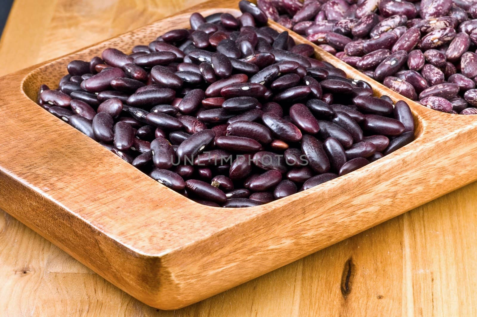 A couple of dark red and spotted kidney beans in wooden dish 