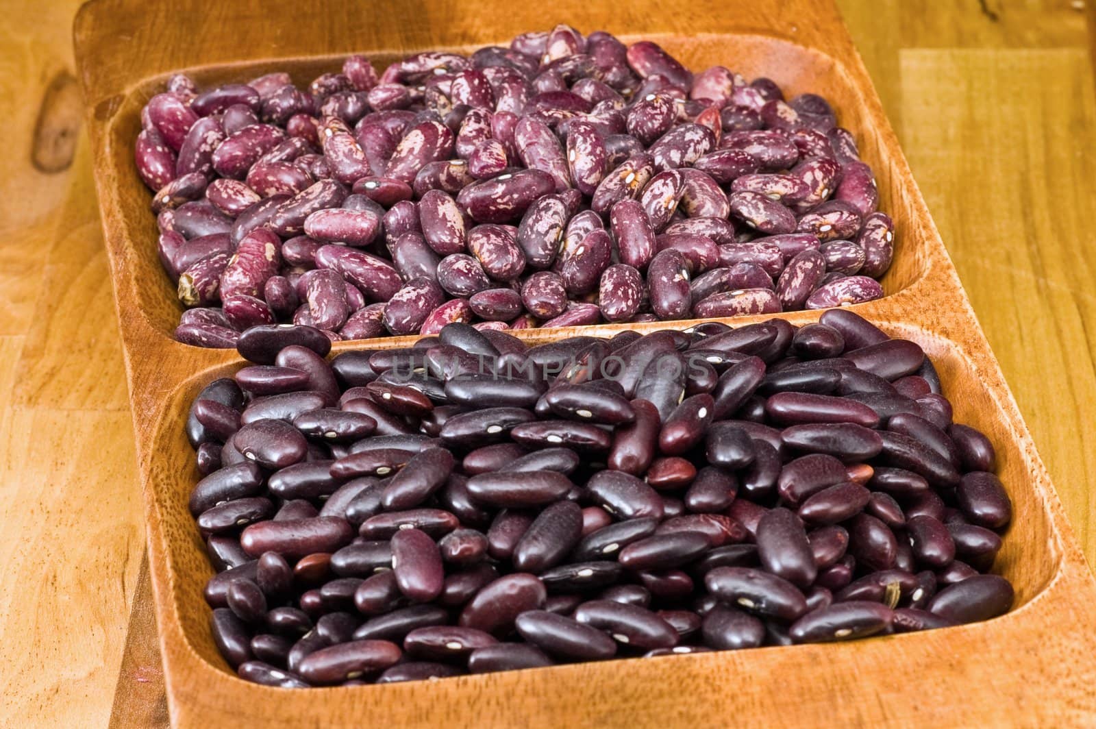 A couple of dark red and spotted kidney beans in wooden dish 