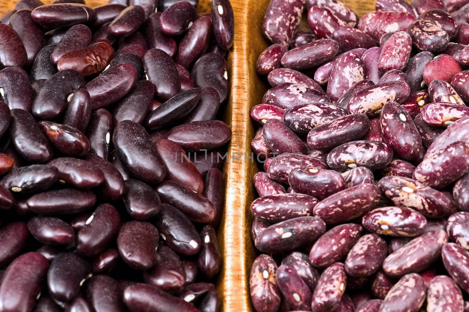 A couple of dark red and spotted kidney beans in wooden dish 