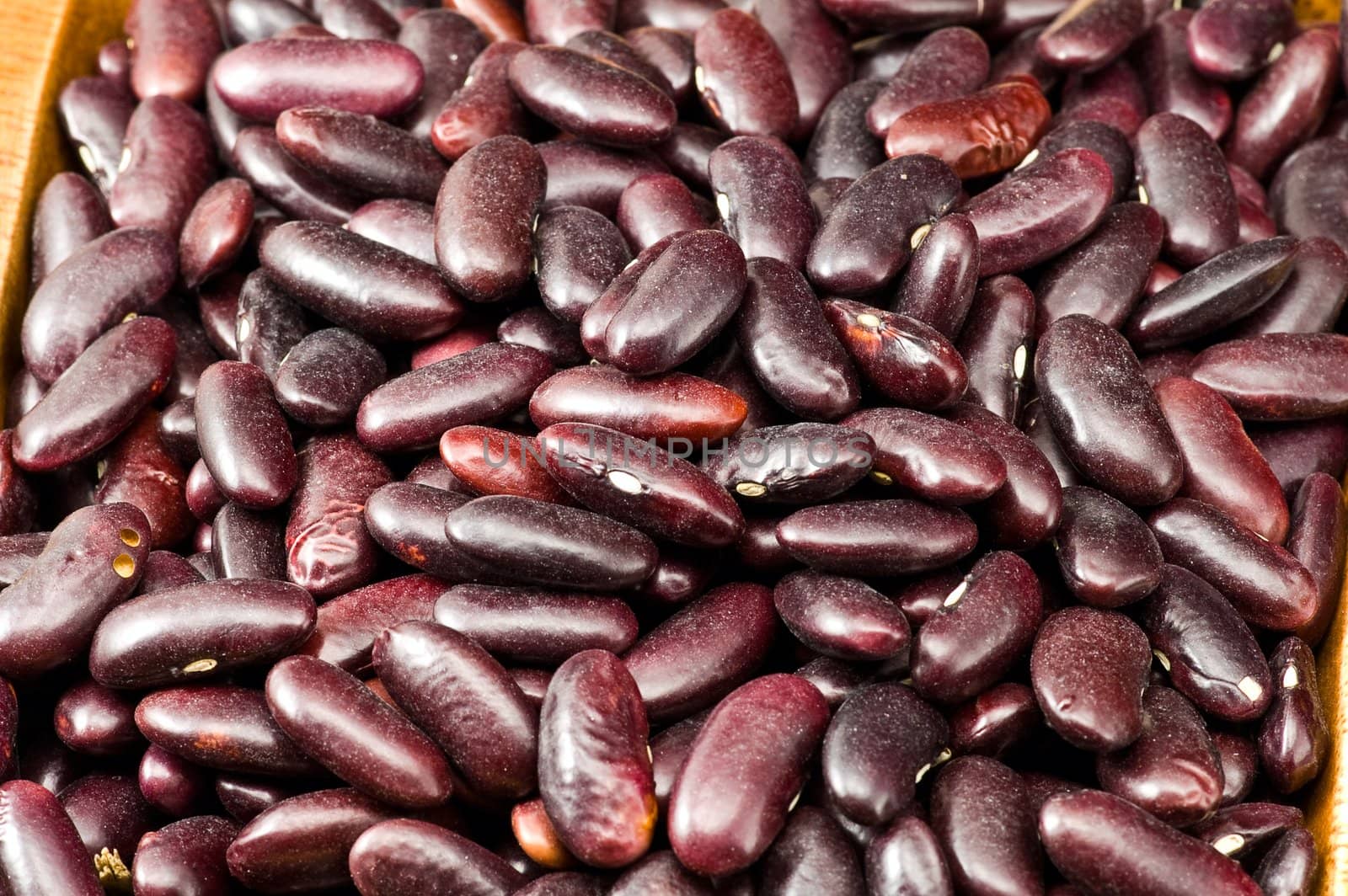 A couple of dark red and spotted kidney beans in wooden dish 