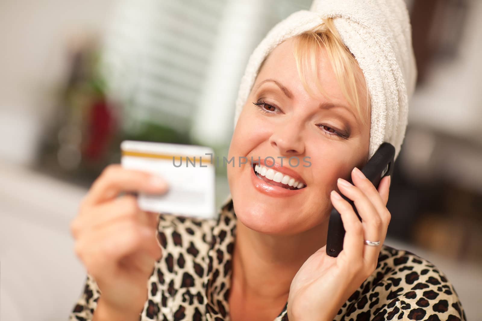 Smiling Robed Woman on Cell Phone Looking At Her Credit Card.