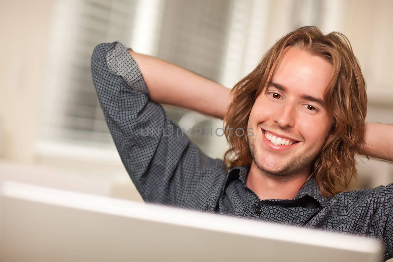 Happy Young Man Using A Laptop Computer with Hands Behind His Head.