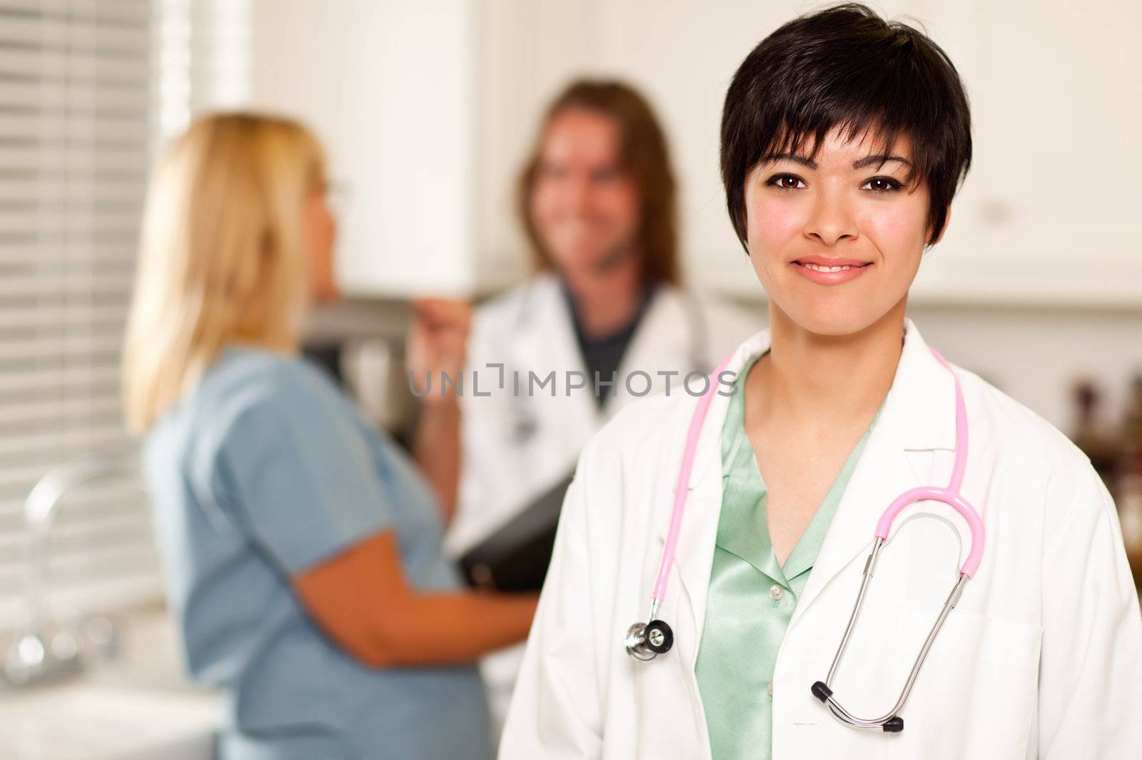 Pretty Latino Doctor Smiles at the Camera as Colleagues Talk Behind Her.