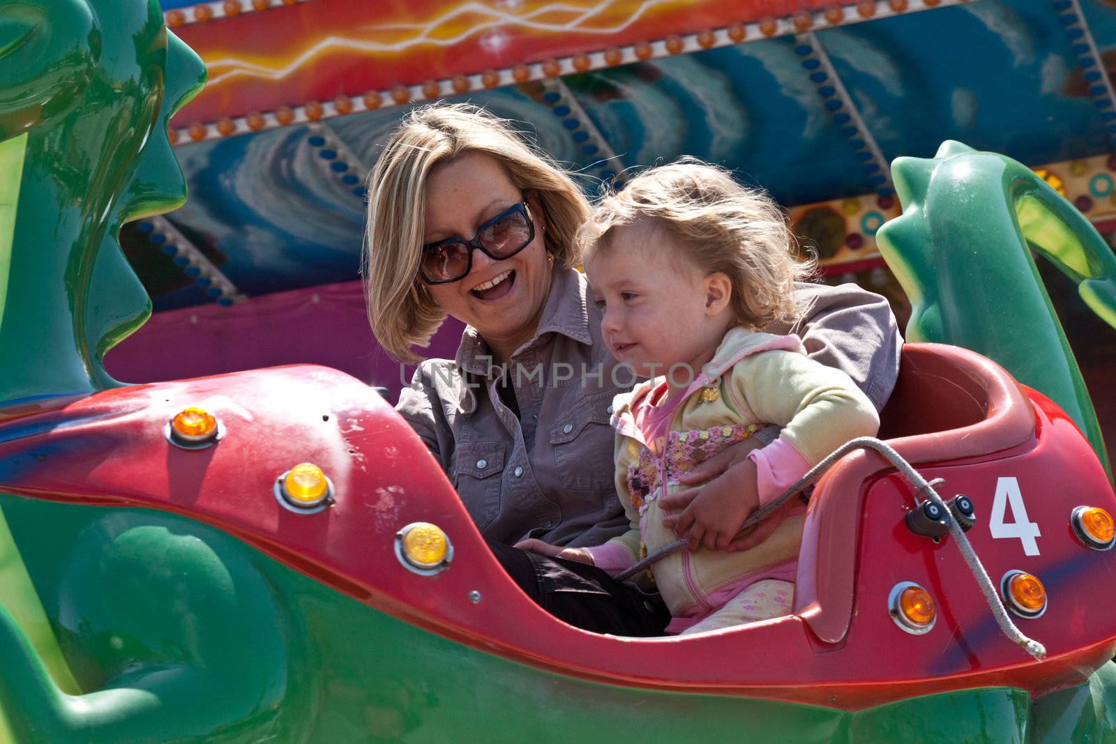 Mother and little daughter having fun rinding on carousel.