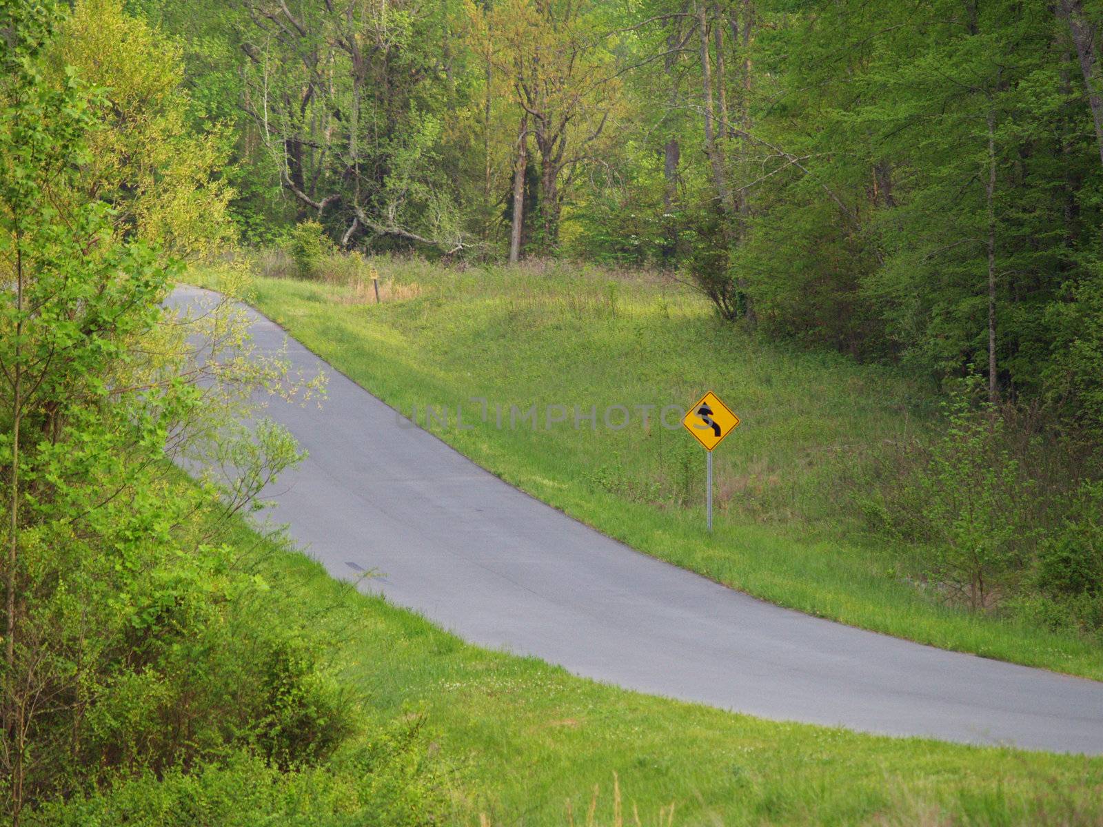 A mountain road in a valley with a curve warning sign